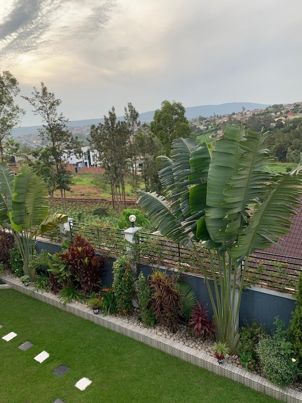 Un jardin aménagé avec une variété de plantes, un chemin pavé et une vue sur une ville lointaine.