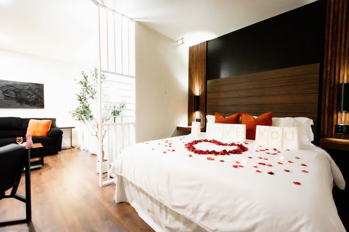 A hotel room with a large bed, a sitting area with a sofa and armchair, and a decorative plant.