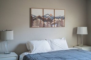 A hotel room with a bed, two bedside tables, a lamp on each table, and a wall-mounted artwork depicting mountains and trees. - Family and Pet Friendly, Hot Tub, Buena Vista (Buena Vista)