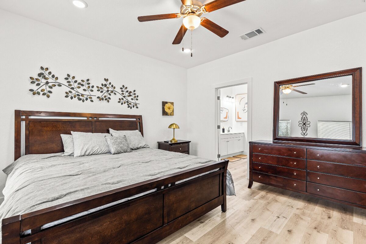A bedroom with a wooden bed, a ceiling fan, a dresser, a mirror, and a wall decoration.