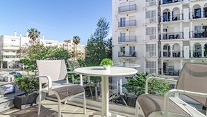 Un balcon avec une table ronde et deux chaises, donnant sur un paysage urbain avec des immeubles et des palmiers.