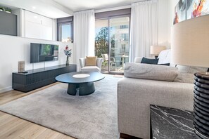 A modern living room with a flat-screen TV, a round coffee table, a sofa, and a dining area with chairs. - Zaga2c - Brand New Modern Apartment 200m to Beach (Estepona)