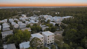A residential area with multiple houses, some with visible balconies, surrounded by trees and a view of the ocean at sunset. - Graytness by Avantstay Sleeps 32 Private Pool + Spa Golf Carts + Bikes Near Beach + Seaside (Santa Rosa Beach)