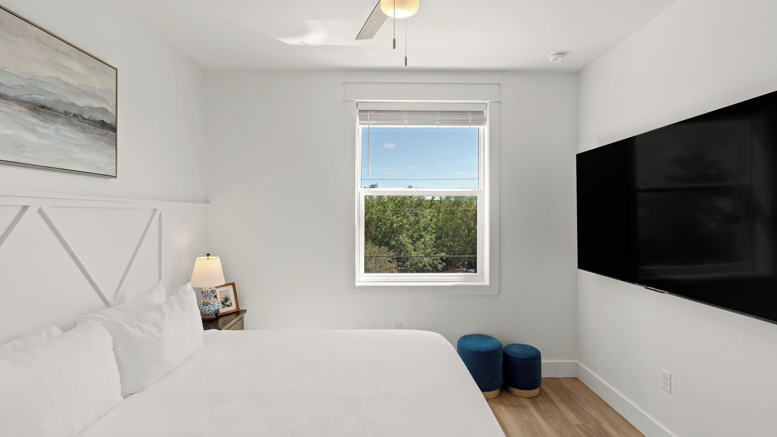A bedroom with a bed, a nightstand, a lamp, a window with a view, and a TV.