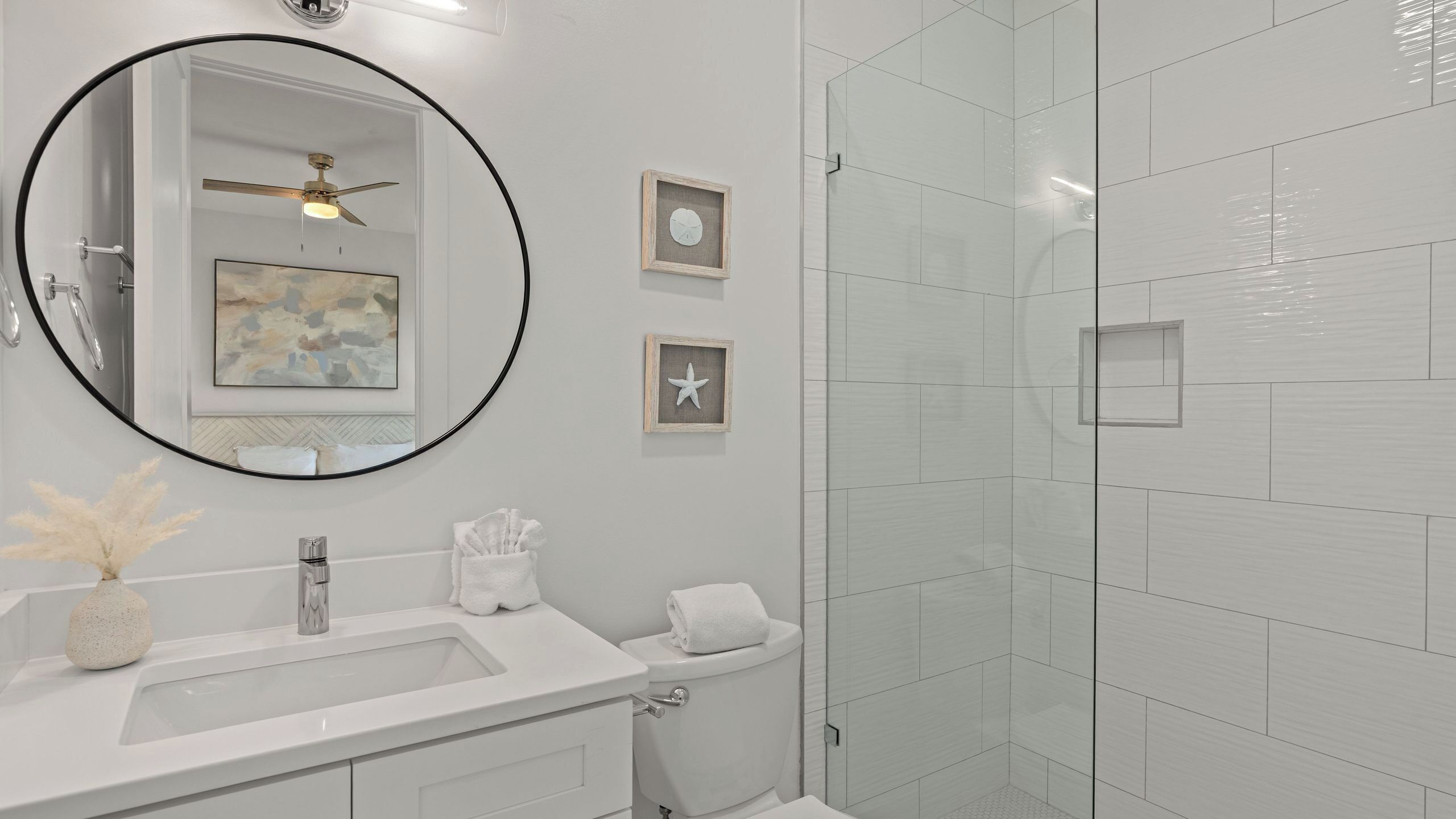 Een moderne badkamer met een grote spiegel, een plafondventilator, een douche en een wastafel.