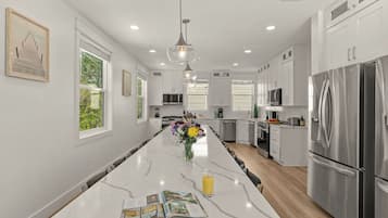 Une cuisine moderne avec des meubles blancs, un îlot en marbre, des appareils électroménagers en acier inoxydable et des luminaires suspendus.