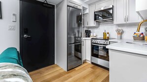 Uma cozinha compacta com geladeira preta, forno de aço inoxidável e armários brancos.