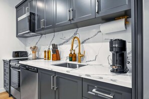 A modern kitchen with grey cabinets, a white countertop, a gold faucet, a coffee machine, and a dishwasher. - The Mccaul Urban Retreat Near Kensington Market (Toronto)