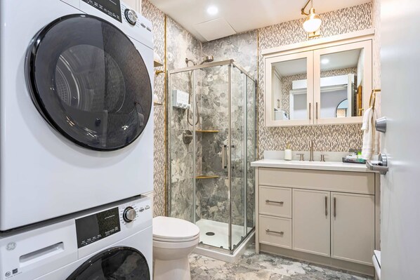 A bathroom with a washing machine, a glass-enclosed shower, a toilet, and a vanity with a mirror. - The Mccaul Urban Retreat Near Kensington Market (Toronto)