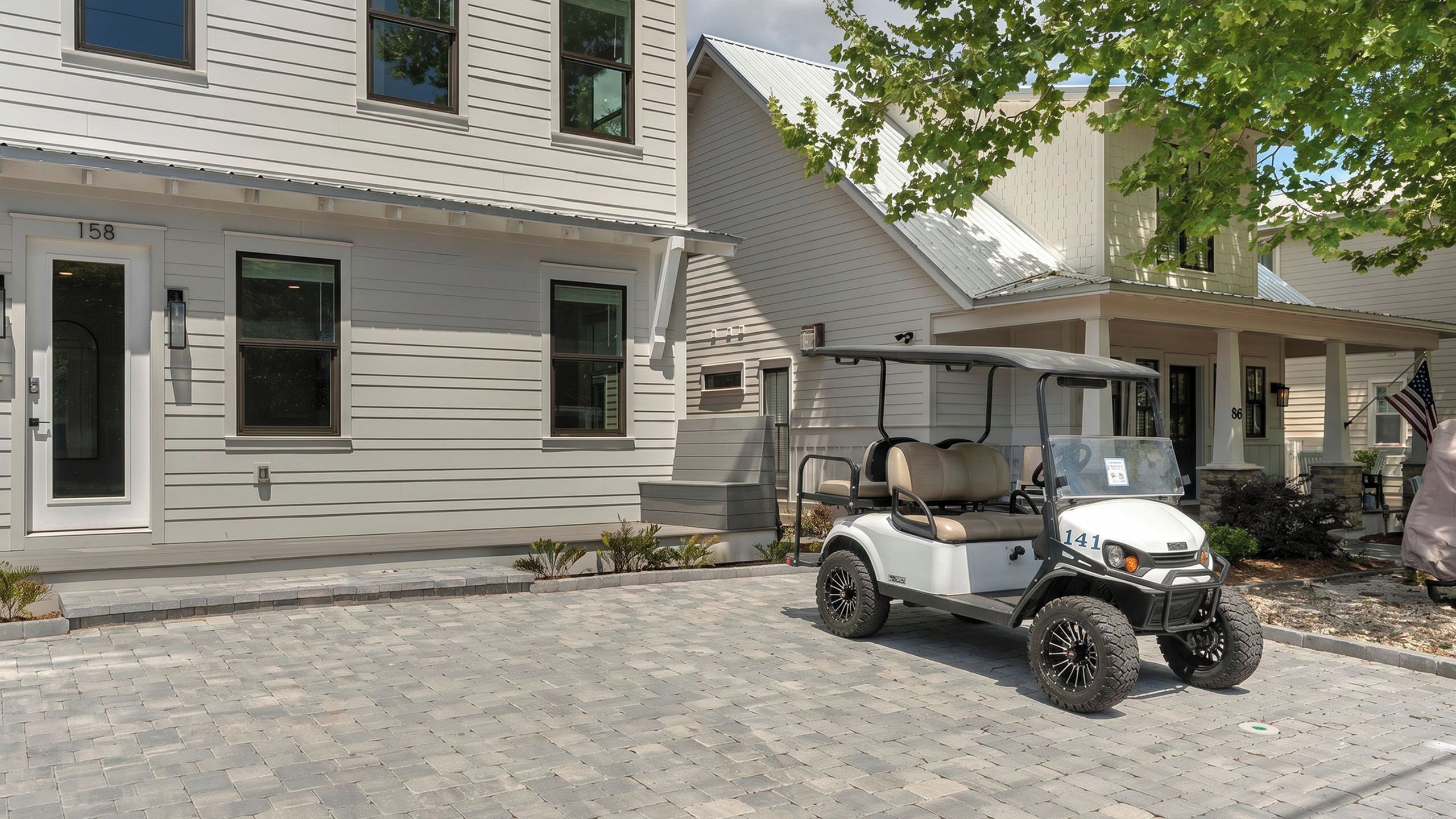 Une maison à deux étages avec une allée pavée, un véhicule de golf garé devant et une boîte aux lettres sur le côté gauche.