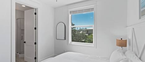 A bedroom with a bed, a window with a view, a door leading to a bathroom, and a bedside lamp.
