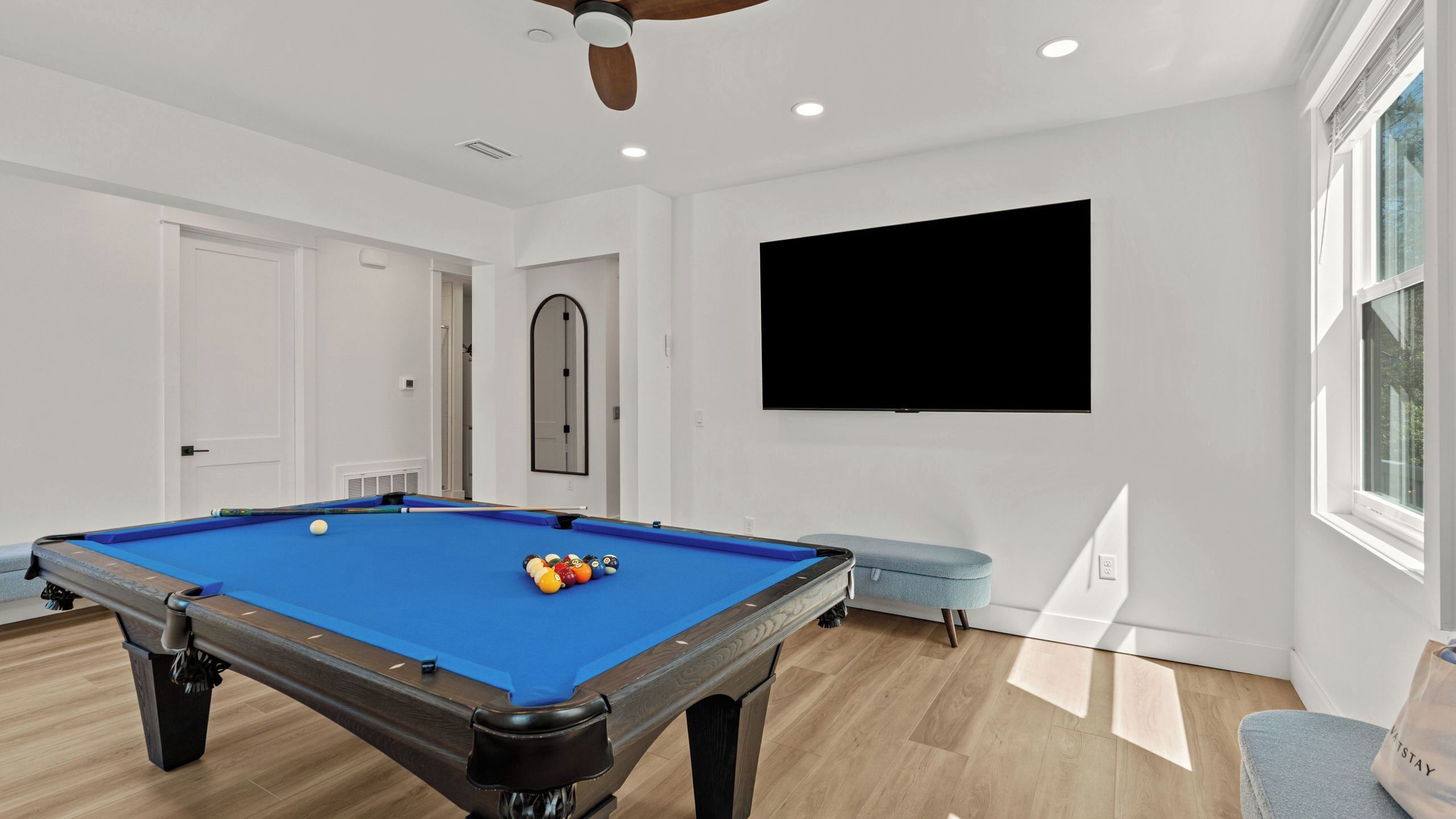 A pool table with balls, a ceiling fan, a TV on the wall, and a window.
