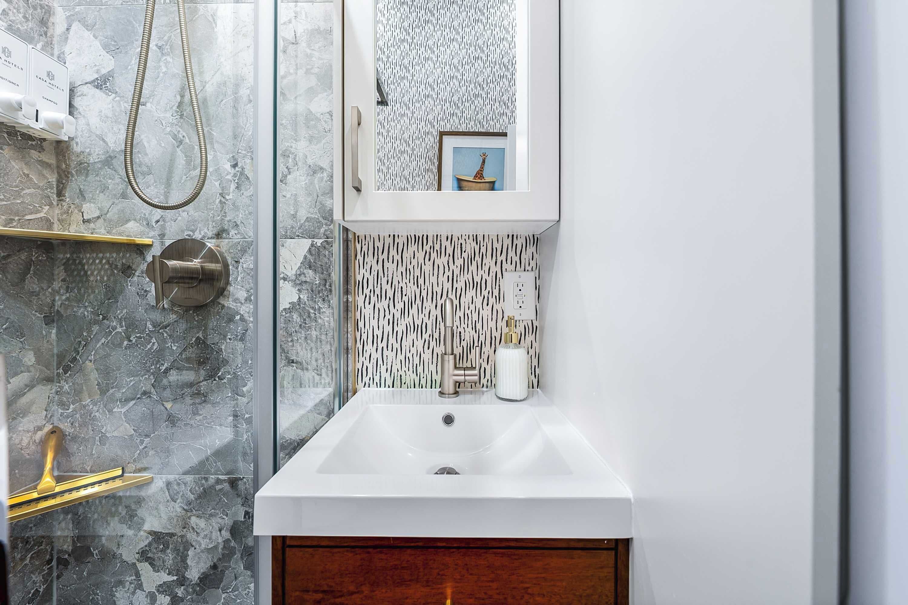 A bathroom with a glass shower enclosure, a white sink, and a marble backsplash.