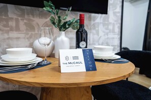 A round wooden table with a wine bottle, a glass, and a welcome sign for The McCAUL Casa Hotels in Toronto. - The Mccaul Basement Near Chinatown & AGO (Toronto)