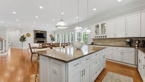 Une cuisine moderne avec des meubles blancs, des plans de travail en granit et des luminaires suspendus.