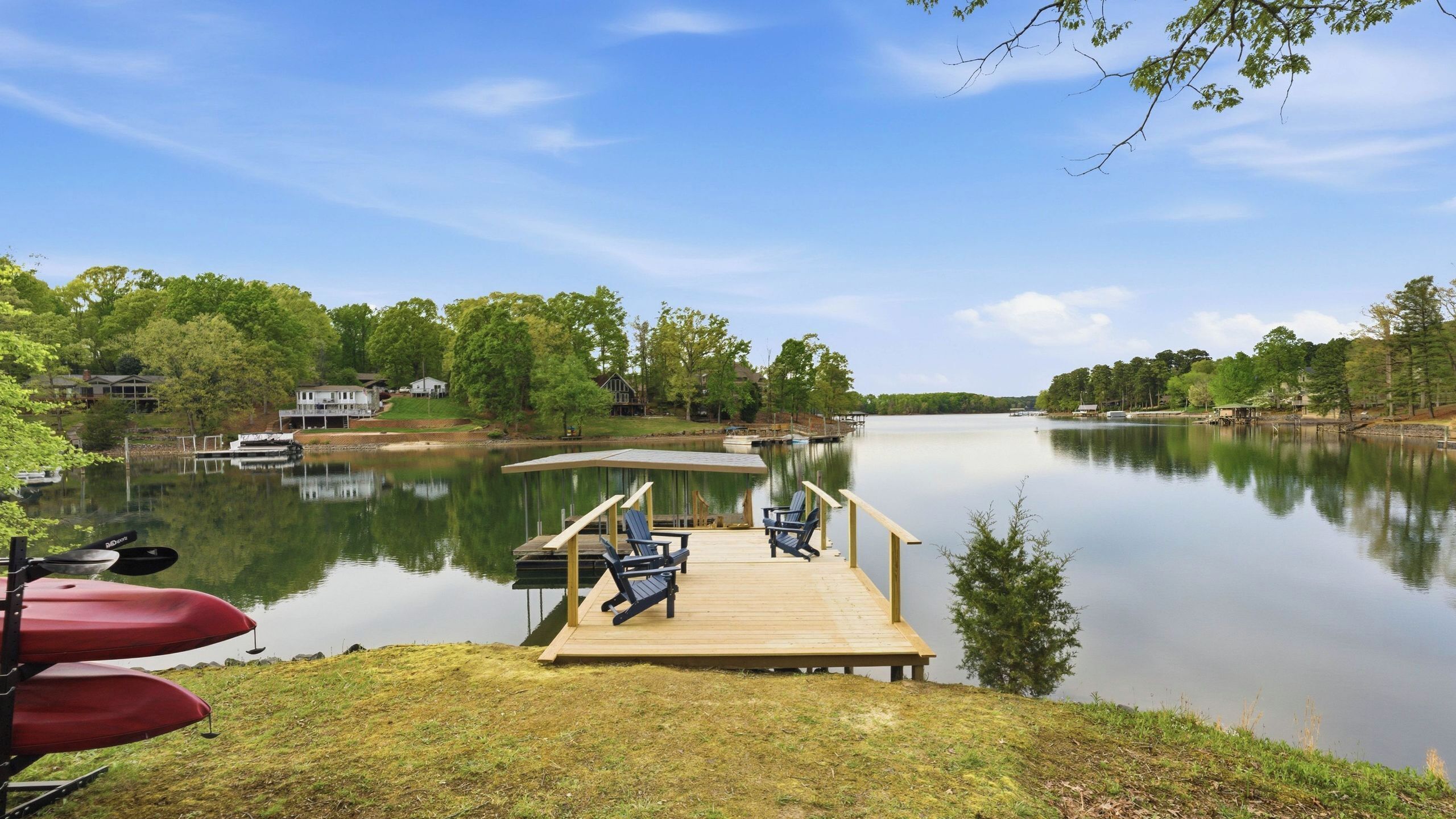 A dock with chairs, a boat, and a calm lake.