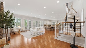Un salon spacieux avec un escalier, un plancher en bois et des meubles blancs.