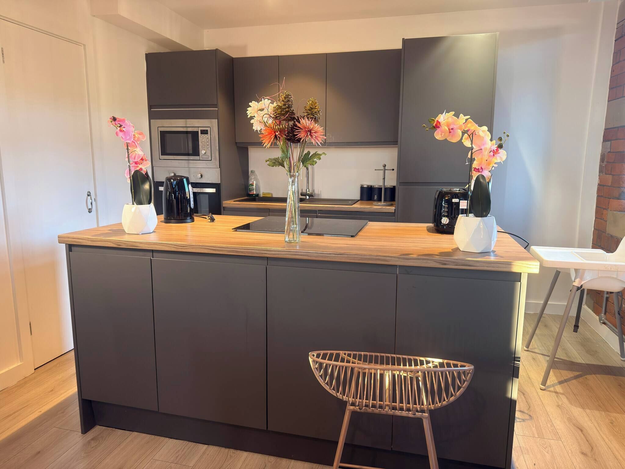 Een moderne keuken met donkere kastjes, een centraal eiland met een bloemenvaas, een magnetron en een koffiezetapparaat.
