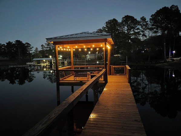 A wooden dock leading to a covered seating area with string lights, overlooking calm water. - Waterfront 3-bedroom house, sleeps 7, pet friendly, boat dock. South Toledo Bend (Burkeville)