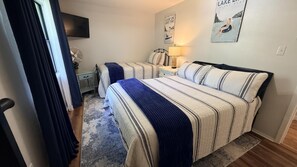 Ein Schlafzimmer mit zwei Betten, einem Fernseher, einer Lampe und einem Poster an der Wand.
