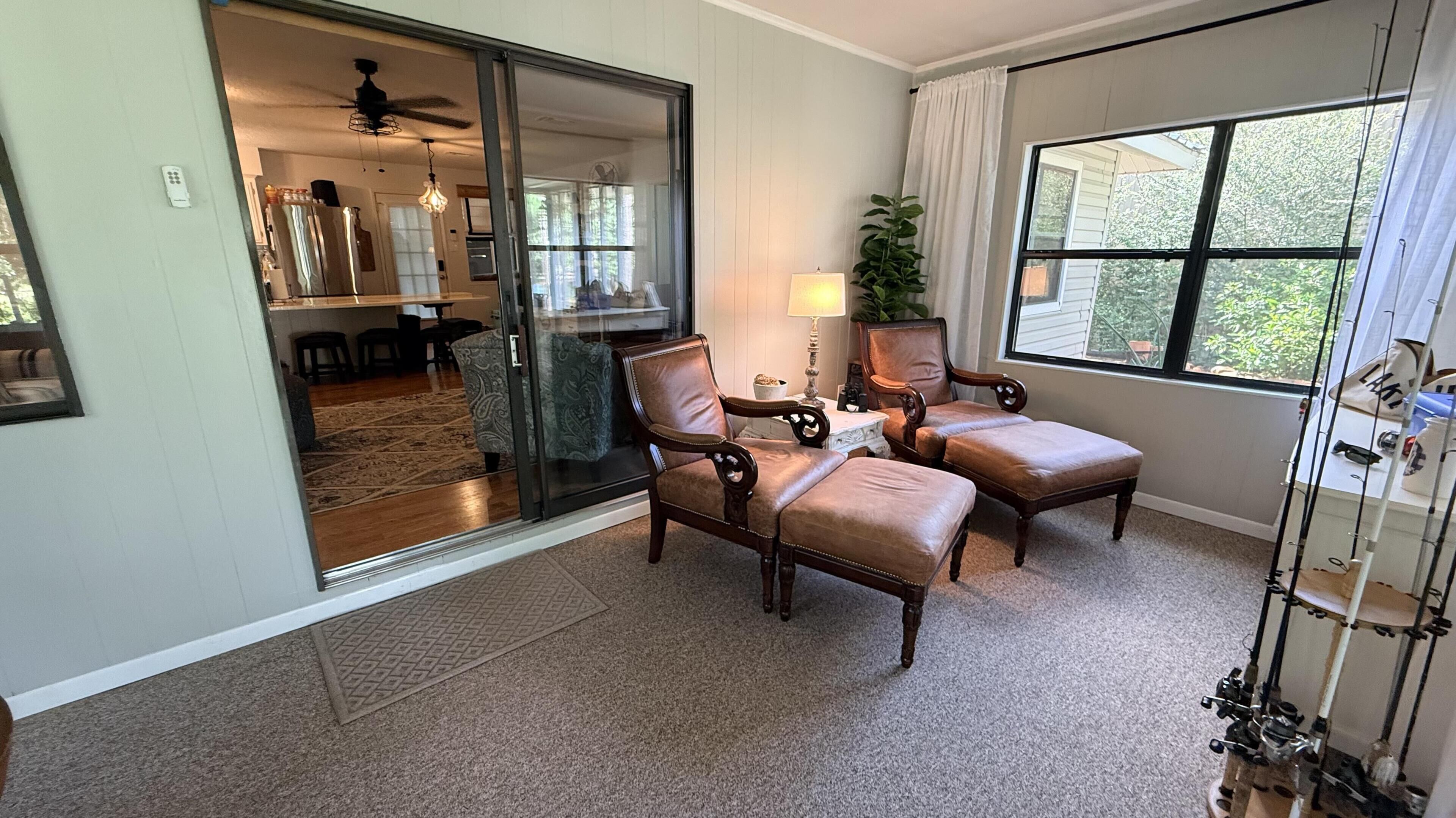 A room with a sliding glass door leading to a dining area, two leather armchairs, a small table with a lamp, and a large window with a view.