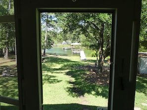 A view through a door of a grassy yard with a dock and a lake.