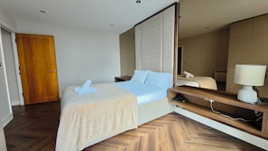 A hotel room with a bed, a bedside table, a mirror, and a wooden door. - Canary Wharf Views, City Soul — Your Waterfront Escape Awaits (London)