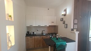 Cocina compacta con armarios blancos, encimera negra y un taburete pequeño.