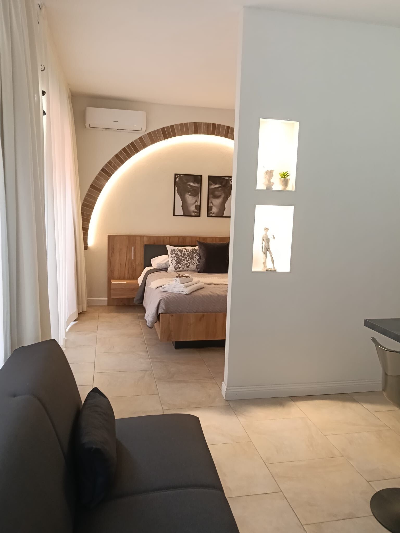 A modern bedroom with a curved ceiling, a bed with a wooden headboard, and a small bedside table.