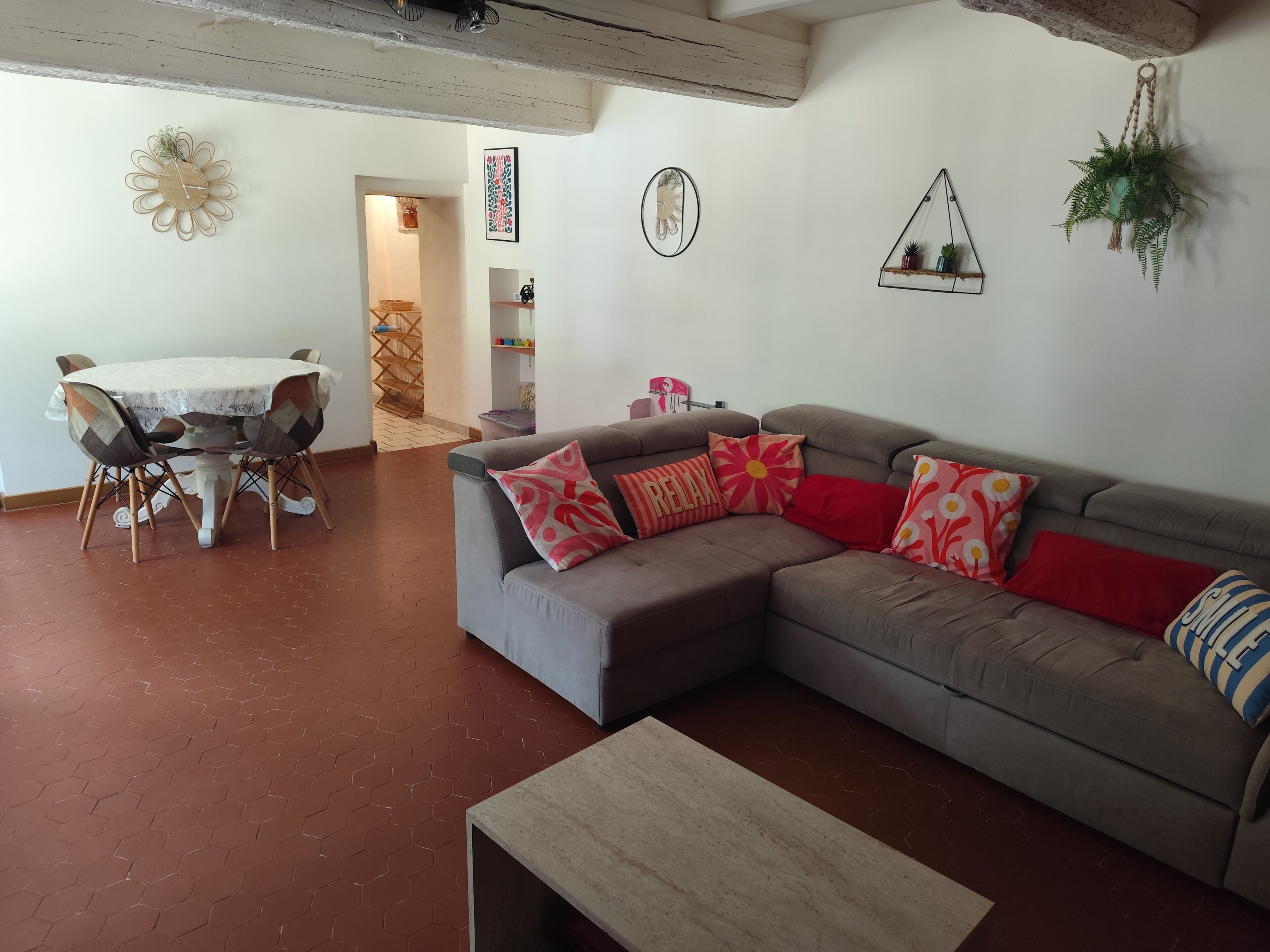 Een woonkamer met een grijze bank, een houten salontafel, en een eethoek met een tafel en stoelen.