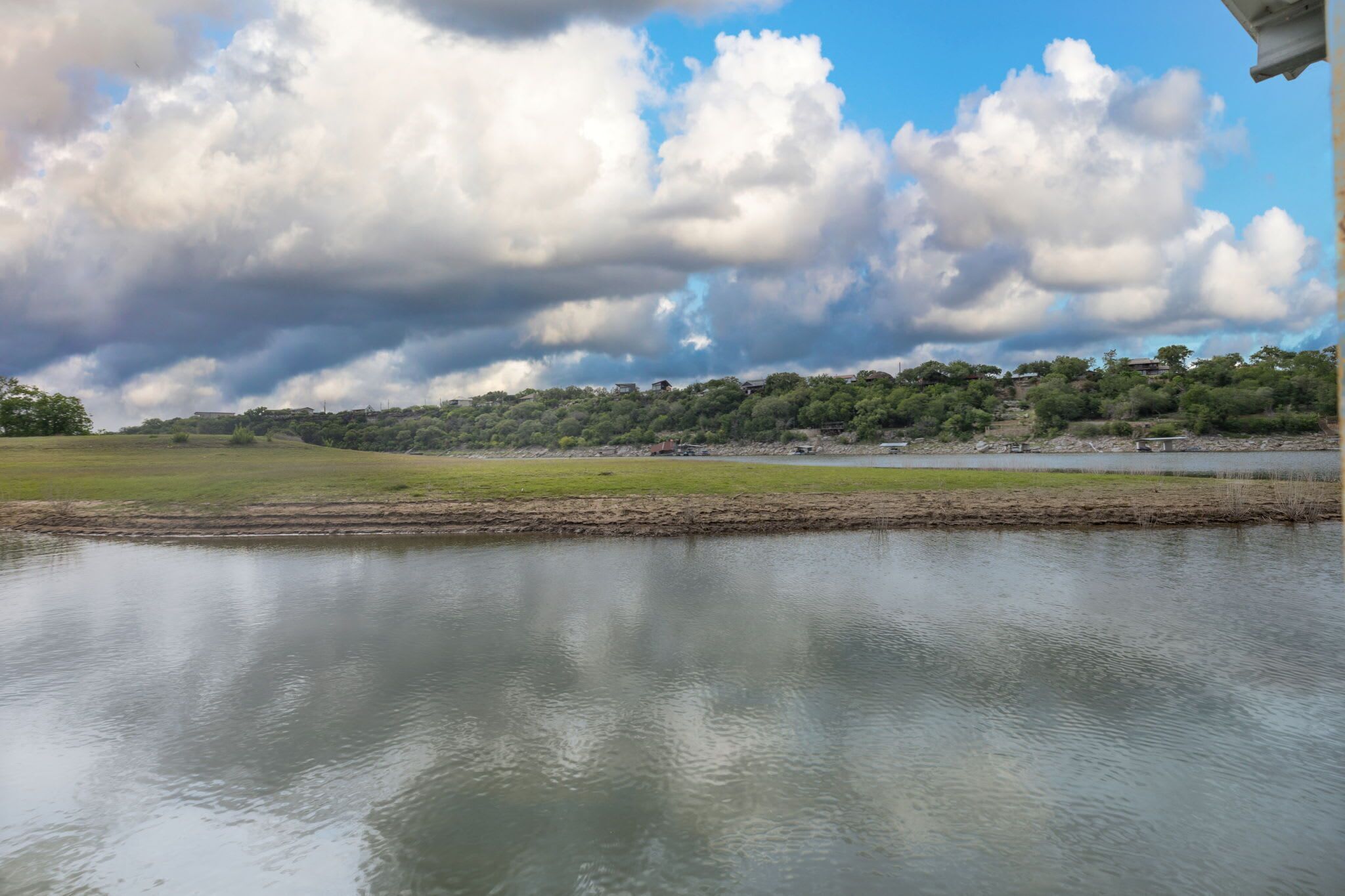Um lago tranquilo com margem gramada, linha distante de árvores e céu parcialmente nublado.
