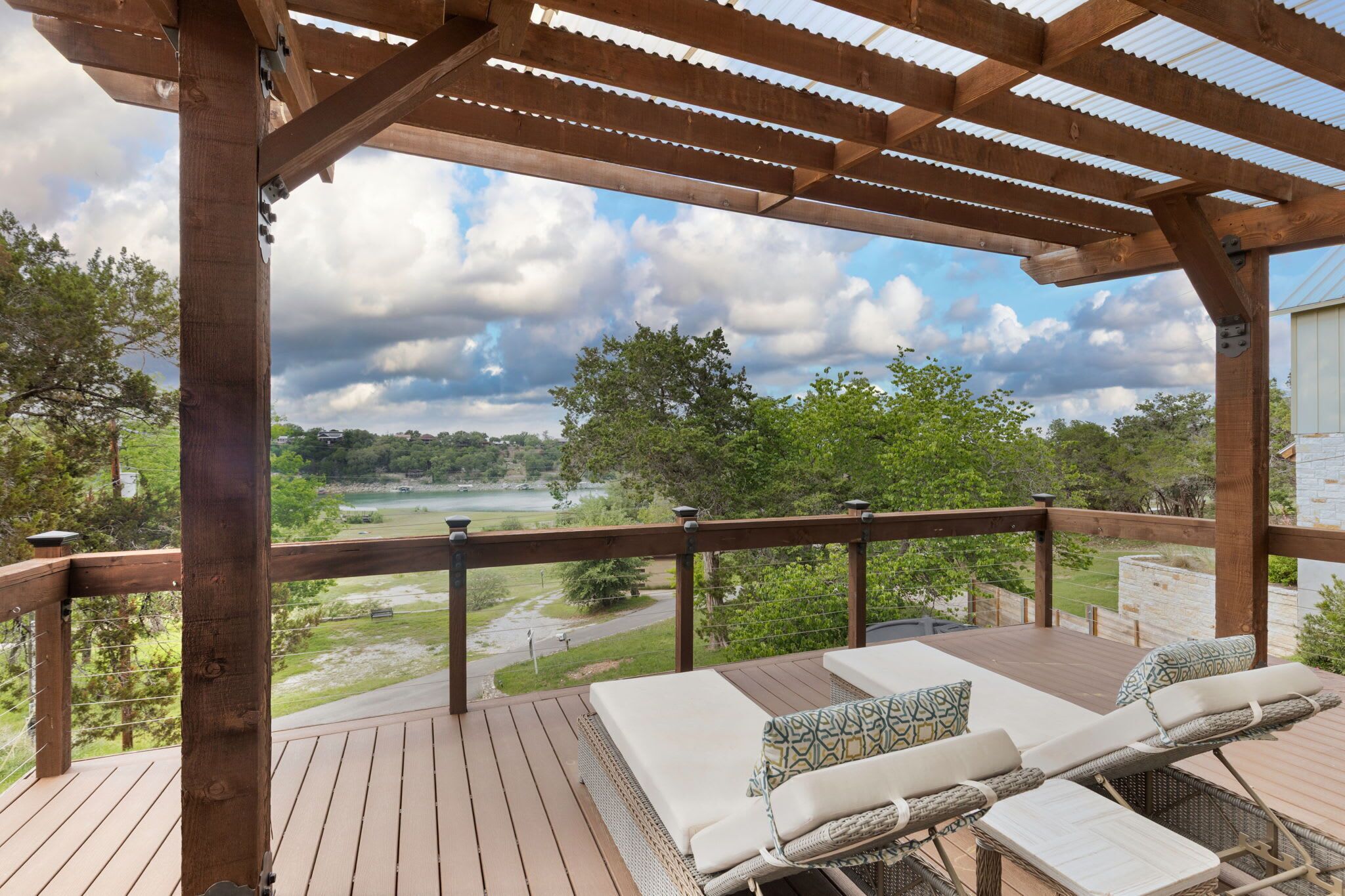 A wooden deck with lounge chairs and a pergola, overlooking a lake and greenery.