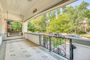 Eine überdachte Veranda mit einer Bank, einem Fliesenboden und Blick auf die Straße und Bäume.