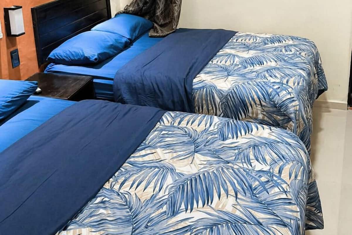 Une chambre avec deux lits, une fenêtre avec des rideaux et un luminaire fixé au mur.