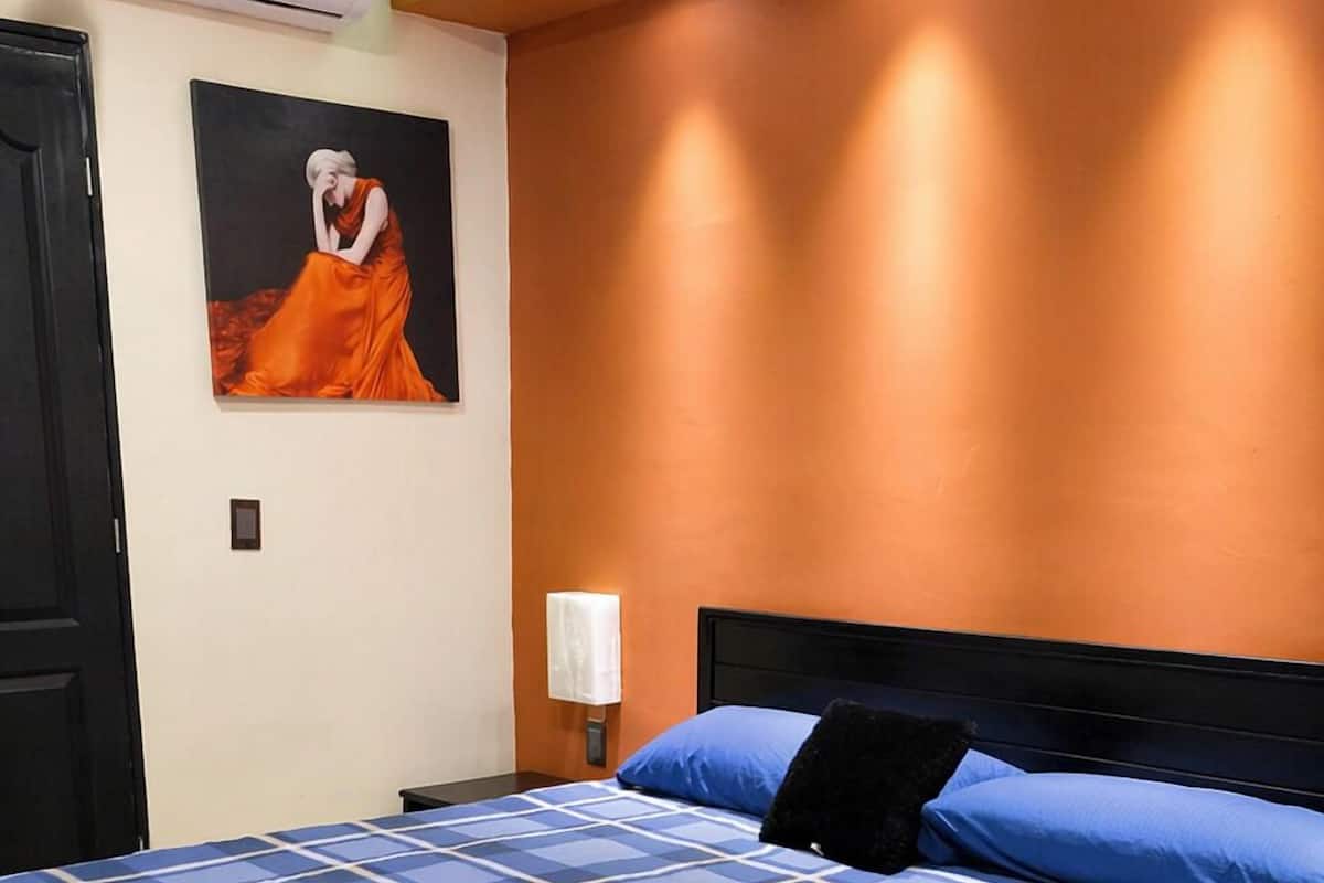 Une chambre à coucher avec un lit, un climatiseur fixé au mur, un tableau et une lampe de chevet.