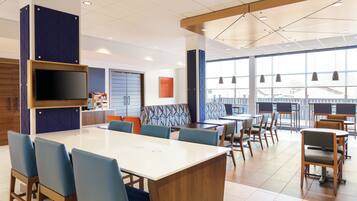 A modern hotel lobby with a large dining area, a flat-screen TV, and large windows.