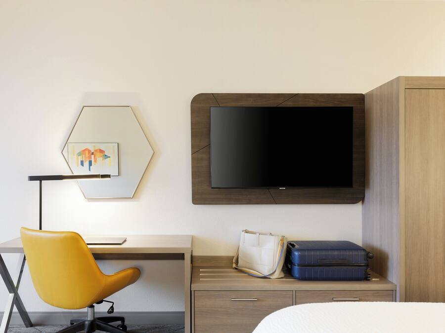 Une chambre d’hôtel équipée d’un bureau, d’une chaise jaune, d’une télévision, d’un lit et d’une armoire.
