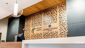 Uma receção com design moderno, uma parede de painéis de madeira com padrões geométricos, e o logótipo Holiday Inn Express Candlewood Suites.