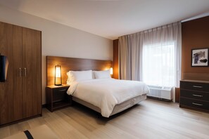 Habitación de hotel con cama, mesitas de noche, armario, radiador y ventana con cortinas.