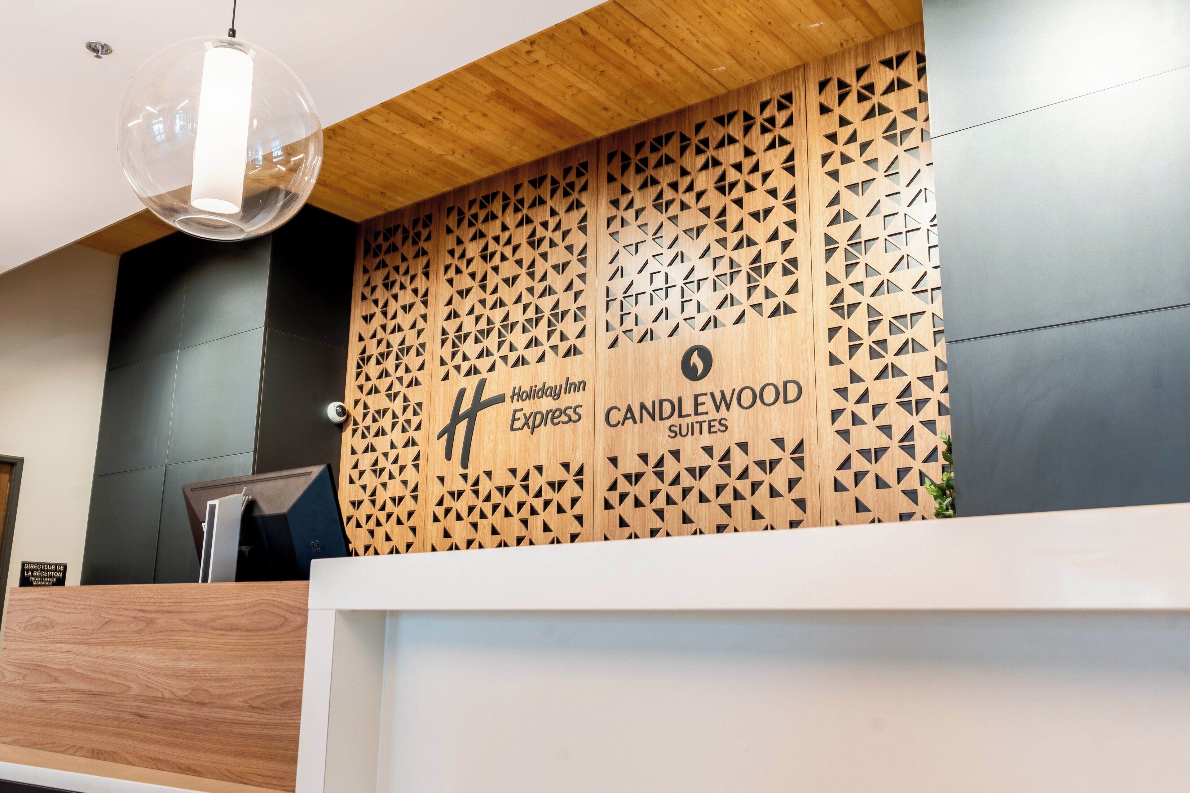 Un mostrador de recepción con diseño moderno, que incluye un panel de pared de madera con patrones geométricos y el logotipo de Holiday Inn Express Candlewood Suites.