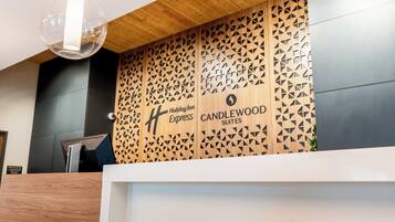 Un mostrador de recepción con diseño moderno, que incluye un panel de pared de madera con patrones geométricos y el logotipo de Holiday Inn Express Candlewood Suites.