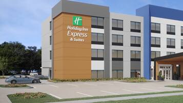 A Holiday Inn Express & Suites building with a modern design, parking lot, and a car in the foreground.