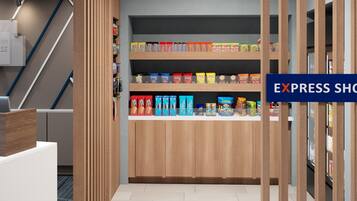 Un pasillo moderno de hotel con un mostrador de recepción de madera, una escalera y un bar de aperitivos con diversos productos envasados.