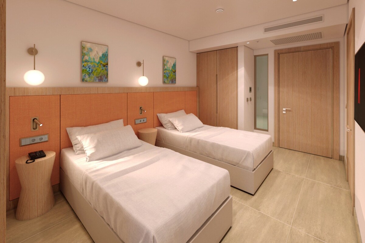 Ein Hotelzimmer mit zwei Betten, einem Nachttisch mit Telefon, einer Wandlampe und einer Tür mit Fensterteil.