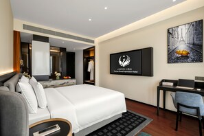 Ein modernes Hotelzimmer mit einem großen Bett, einem Schreibtisch, einem Sessel, einem Flachbildfernseher und einem gerahmten Bild vom Eiffelturm.