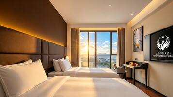 A hotel room with two beds, a desk, and a large window with a city view.