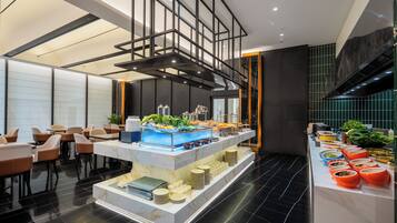 Un vestíbulo de hotel moderno con una zona de buffet central, arreglos de asientos y una escalera.