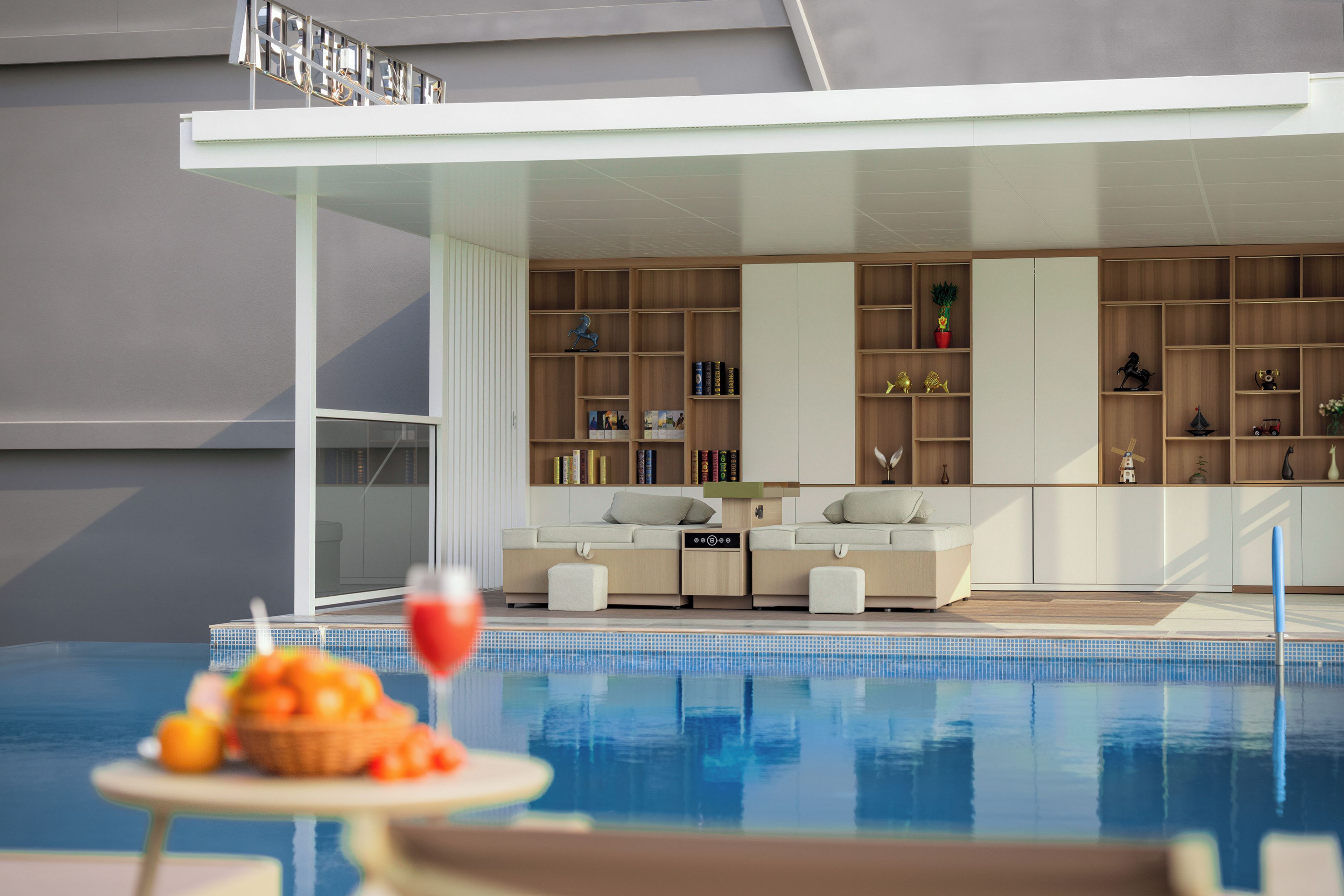 A modern indoor pool area with a seating area and a bookshelf filled with books and decorative items.