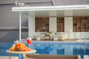 Un área de piscina interior moderna con una zona de estar y una estantería llena de libros y objetos decorativos.