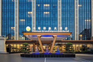 The exterior of Yunnan Grand Impression Hotel with a modern facade, illuminated signage, and a water feature in front.